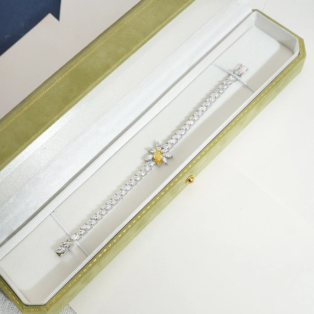 A silver-toned diamond bracelet with a yellow diamond center, displayed inside an open gold velvet jewelry box.
