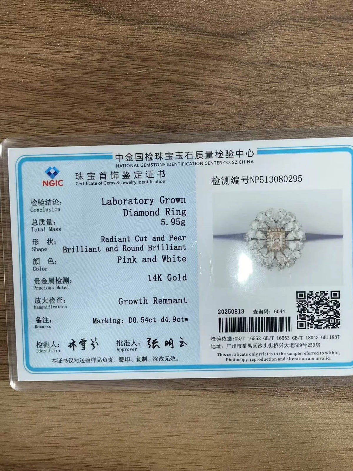 A certificate card for a pink and white 14k gold diamond ring, showing details and a small ring photo, placed on a wooden surface.