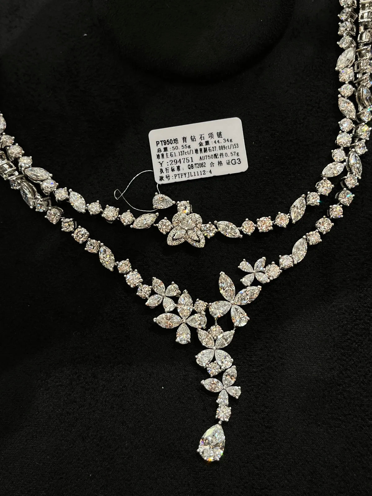 A double-row diamond necklace with a floral and teardrop pendant, displayed on a black velvet background with a product tag attached.