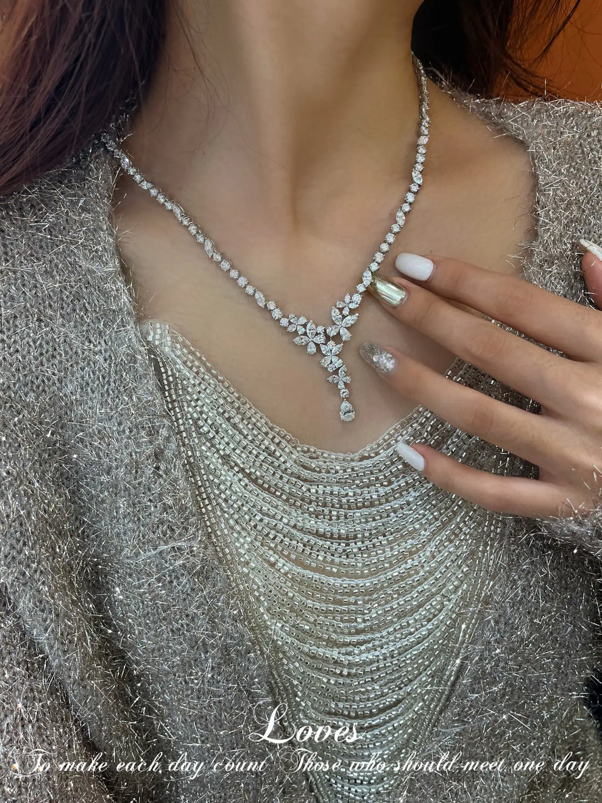 A close-up of a model wearing a sparkling silver rhinestone necklace with a floral pendant, styled over a textured silver top.