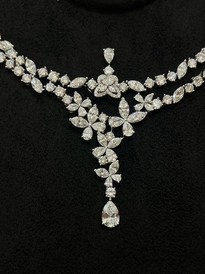 A sparkling silver-tone diamond necklace with a floral and leaf motif, featuring a central teardrop diamond pendant, displayed on a black velvet background.