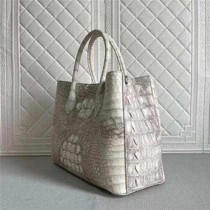 A structured tote bag with a mixed crocodile-embossed texture in light gray and white, featuring dual top handles, set against a textured white paneled wall.