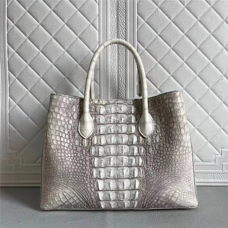 A large structured tote handbag with a metallic silver alligator or crocodile-embossed texture, featuring two top handles and a quilted light gray background.