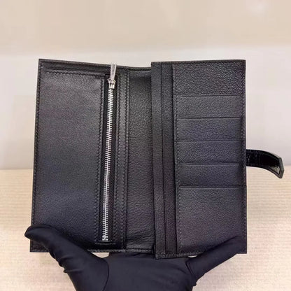 A black textured leather wallet held open by a gloved hand, showing a vertical silver zipper on the left and multiple card slots on the right.