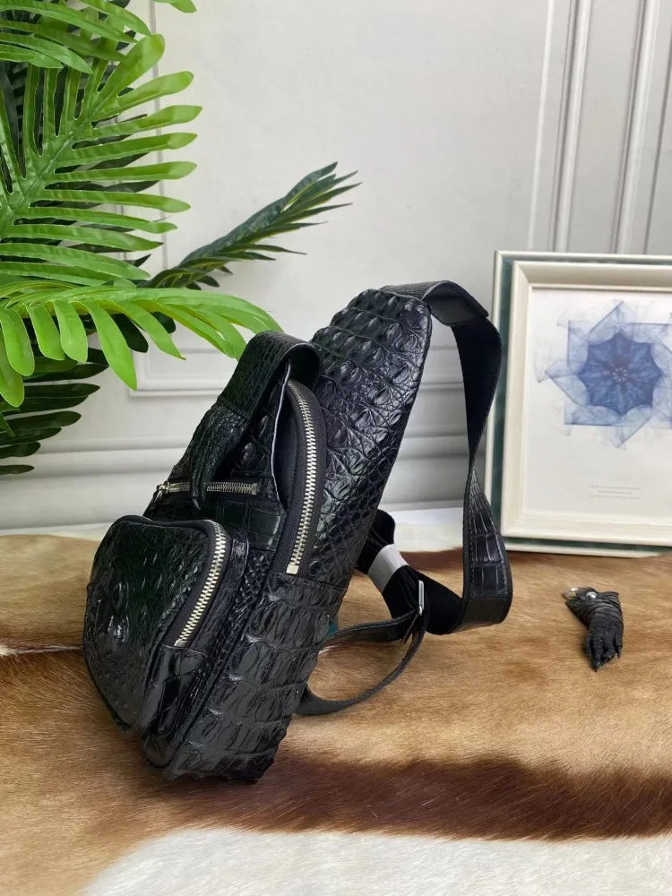 A black crocodile-embossed leather shoulder bag with multiple zippered compartments, displayed on a brown and white cowhide rug next to a green plant and a framed picture.