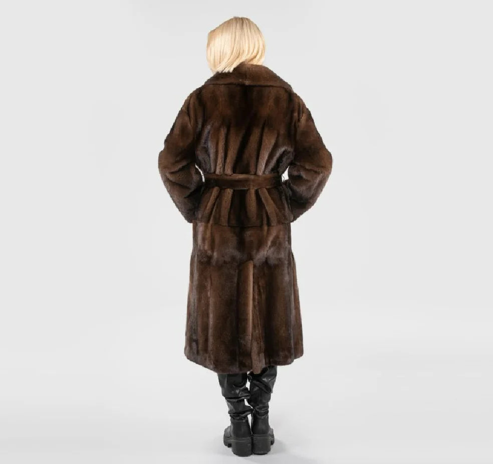 A person shown from the back wearing a long brown fur coat with a matching belt, paired with black boots, against a light gray studio background.