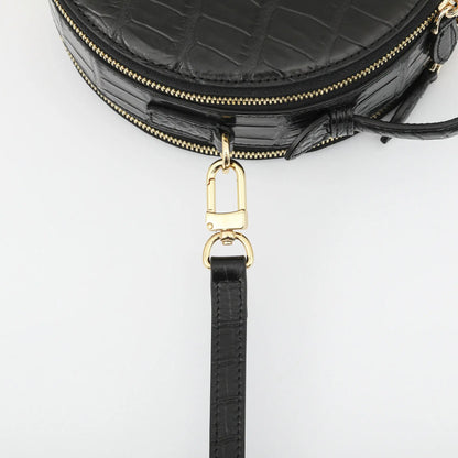 Close-up of a black crocodile-embossed leather handbag with gold-tone hardware and a detachable black leather wristlet strap, shown on a light gray background.