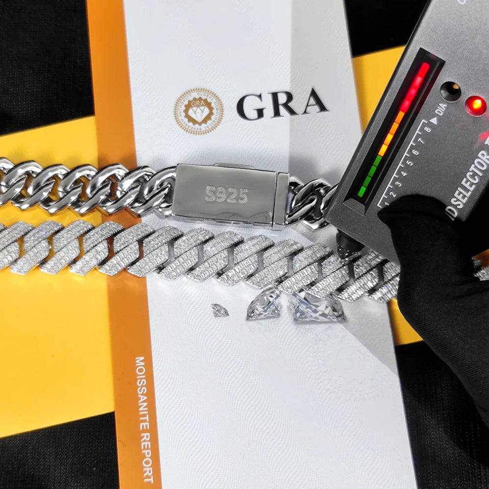 A close-up of a silver Cuban link chain bracelet with pavé-set stones, shown next to a black and yellow Moissanite Report card and a handheld diamond tester. The clasp is engraved with 'S925'.
