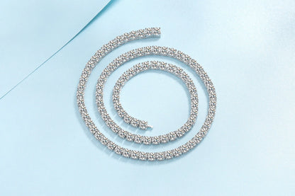 A single tennis-style bracelet with a continuous row of clear rhinestones set in a silver-toned metal, arranged in a spiral on a light blue background.