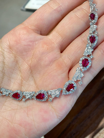 A close-up of a hand holding a silver-toned bracelet featuring multiple oval-cut red gemstones surrounded by small clear stones.