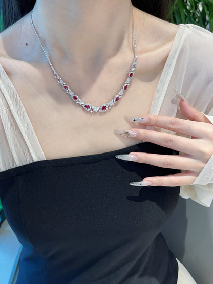 A close-up of a model wearing a delicate silver necklace adorned with small red gemstones, styled with a black and white top.