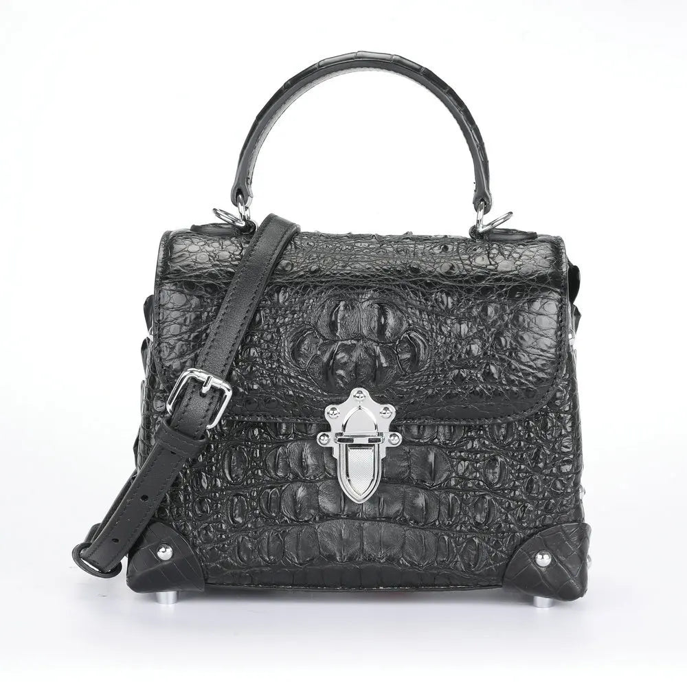 Black crocodile-embossed leather handbag with a top handle, shoulder strap, silver-tone clasp, and protective metal corner guards, shown on a white background.