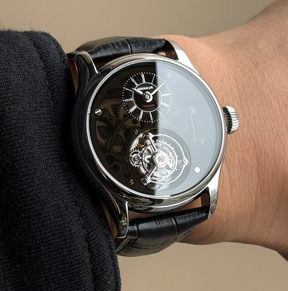 Luxury watch with black leather strap on a wrist against a neutral background