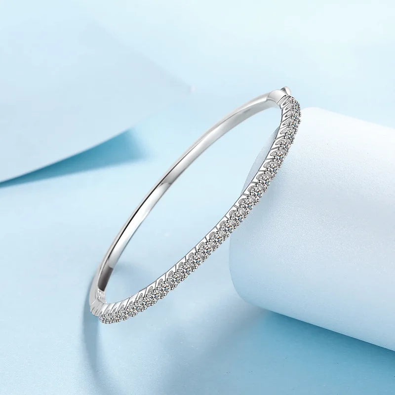 A slim silver bangle bracelet with a textured pavé-set row of clear stones along one half of the band, displayed on a light blue and white background.