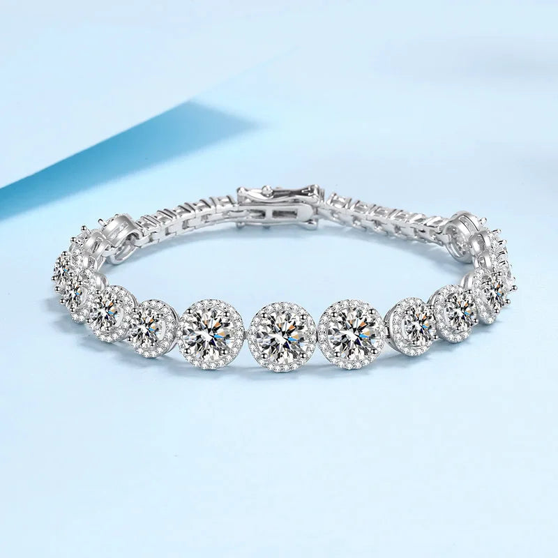 A silver tennis bracelet featuring round diamond halos and a central round diamond, displayed on a light blue background.