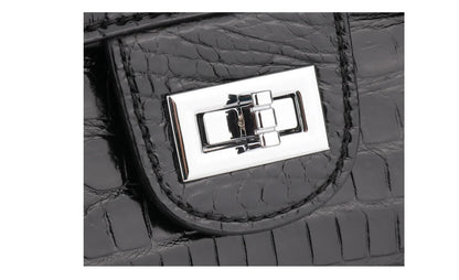 Close-up of a black crocodile-embossed leather handbag featuring a polished silver-tone metal turn-lock clasp on a white background.