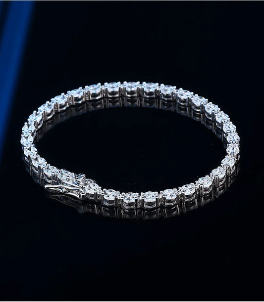 A silver tennis bracelet with a detailed dragon head clasp, set with clear stones and displayed on a reflective black surface.