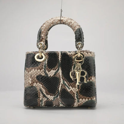 A small structured handbag with a snakeskin pattern in black, beige, and brown, featuring a top handle, gold-tone hardware, and a hanging Christian Dior CD charm.