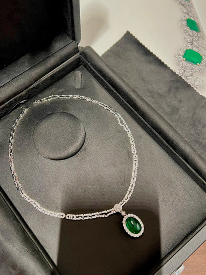 A silver-toned chain necklace with a green oval pendant, displayed inside an open black jewelry box with a gray velvet insert.