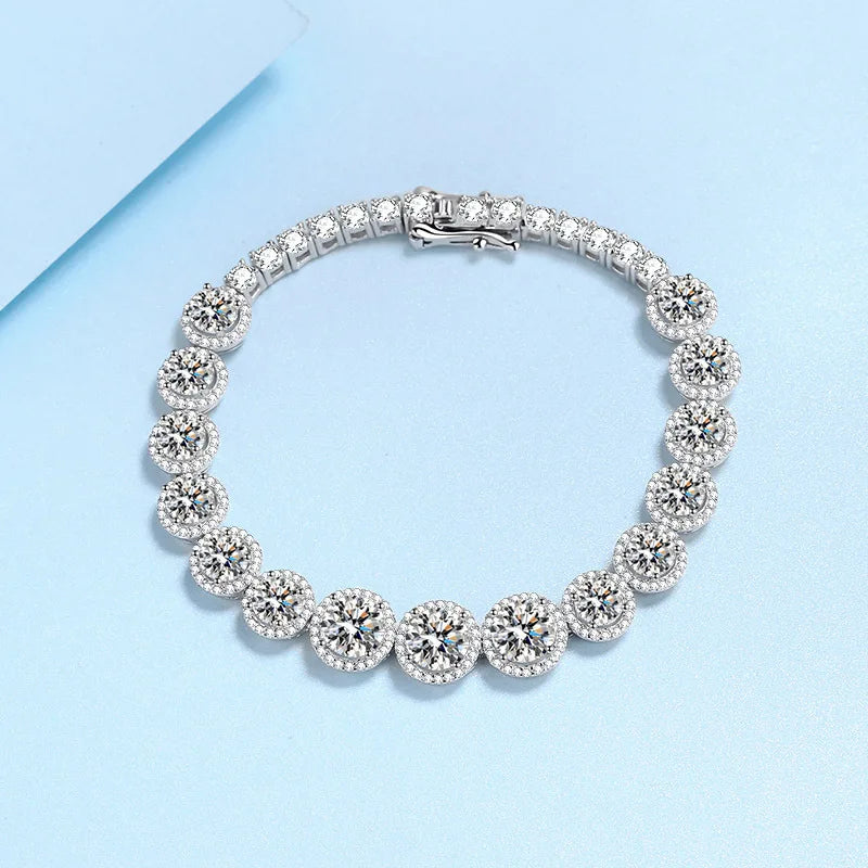 A silver tennis bracelet with round floral cluster settings, photographed on a light blue background.
