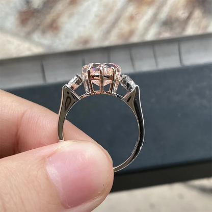 A close-up of a hand holding a rose gold ring with a central pink gemstone and side diamonds, set against a blurred background.