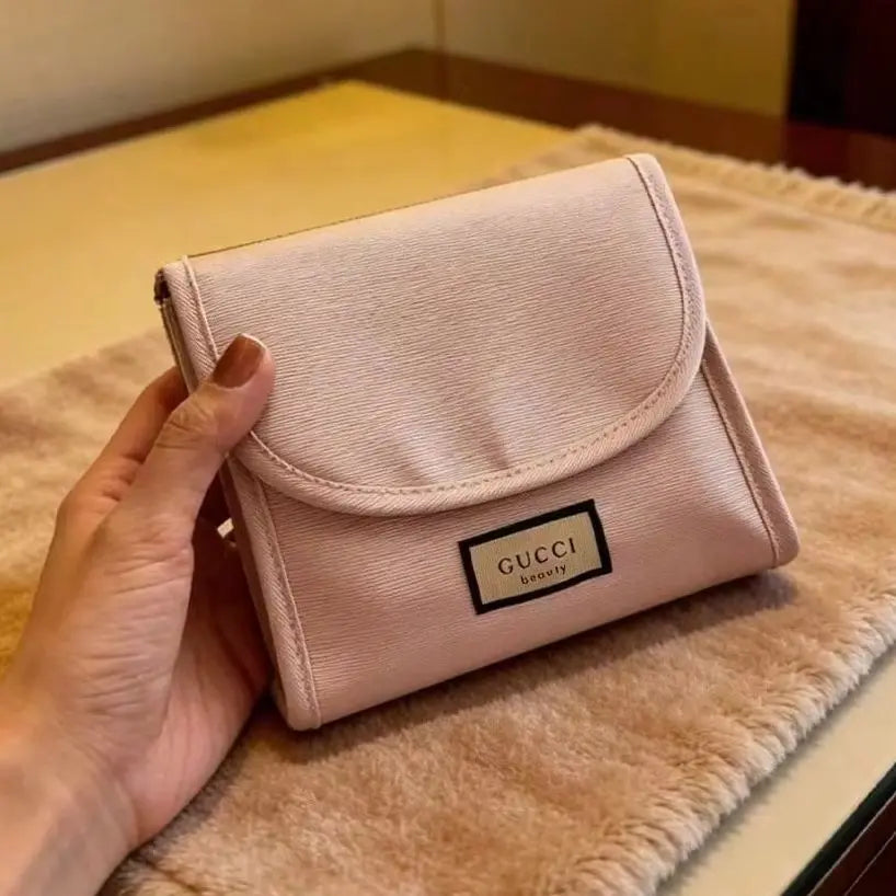 A hand holding a small Gucci wallet in a pale pink textured leather, resting on a beige fuzzy surface.
