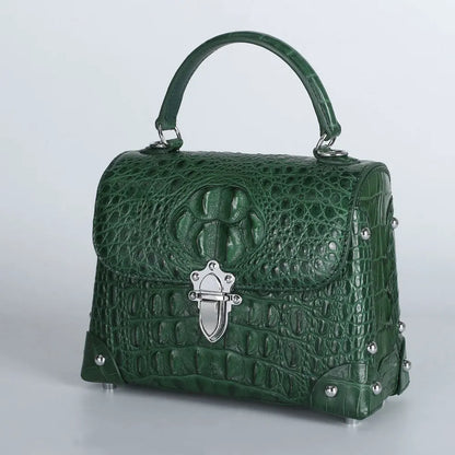 A structured green crocodile-embossed handbag with a top handle, silver-tone hardware, and decorative studs, photographed on a light gray studio background.