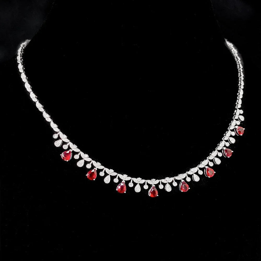 A silver-toned necklace with a row of clear teardrop-shaped stones and alternating red teardrop gemstones, displayed on a black velvet neck stand.