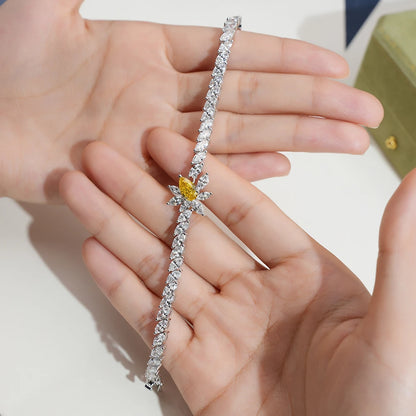 A silver-toned tennis bracelet with a unique star-shaped cluster of clear stones and a central yellow gemstone, held in a person's hands.