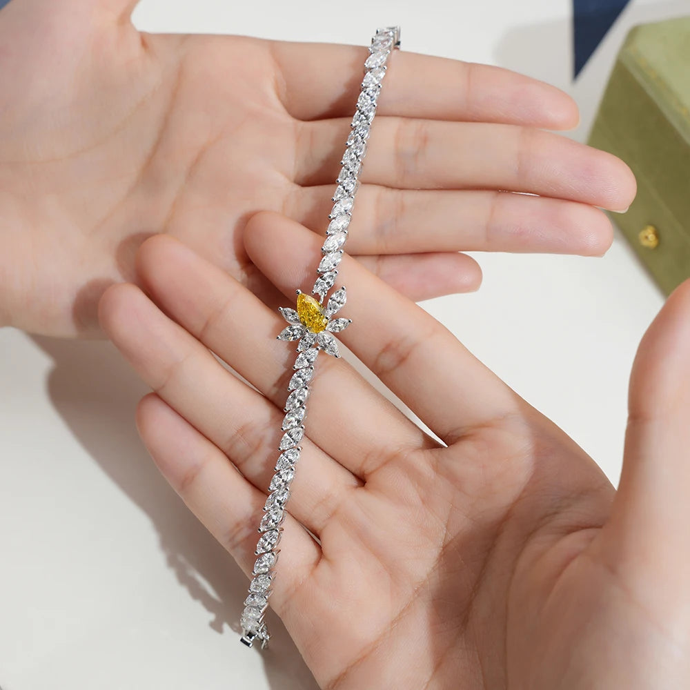 A silver-toned tennis bracelet with a unique star-shaped cluster of clear stones and a central yellow gemstone, held in a person's hands.