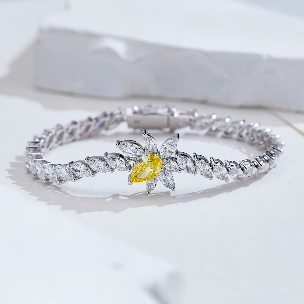 A silver-toned bracelet featuring a central flower motif with clear marquise-cut stones and a prominent yellow center stone, displayed on a light marble surface.