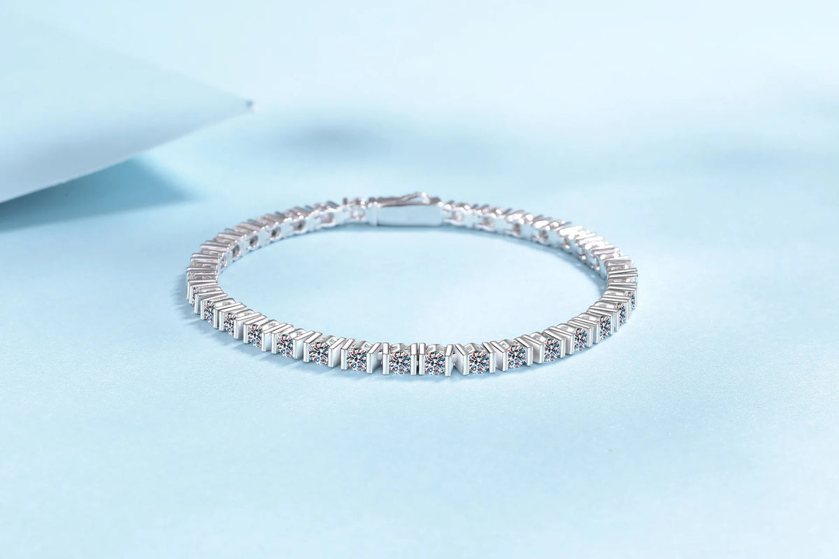 A silver tennis bracelet with clear rectangular gemstones, displayed on a light blue background.