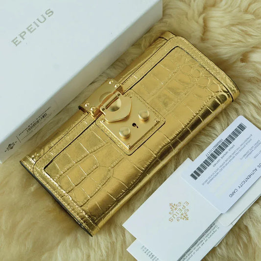 A gold faux-crocodile leather wallet with a padlock clasp, shown next to its white EPEIUS box and authenticity card on a beige faux fur background.