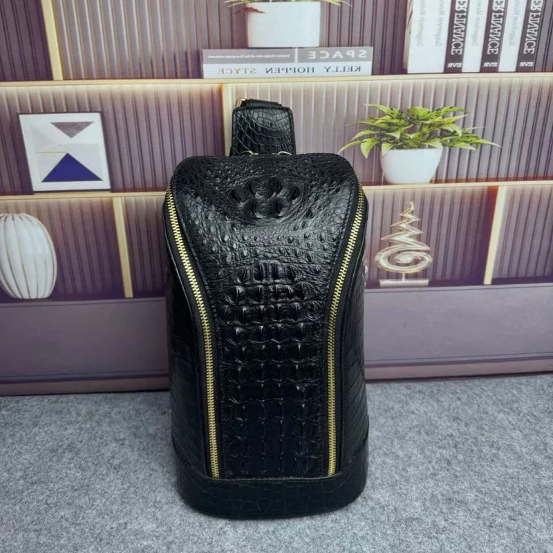 A black crocodile-embossed leather bag with gold zippers, standing upright on a gray carpet in front of a purple-toned bookshelf with books and small plants.