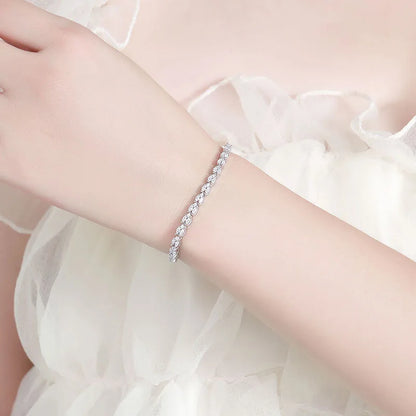 A delicate silver-toned tennis bracelet with clear stones, worn on a woman's wrist against a soft white tulle dress background.