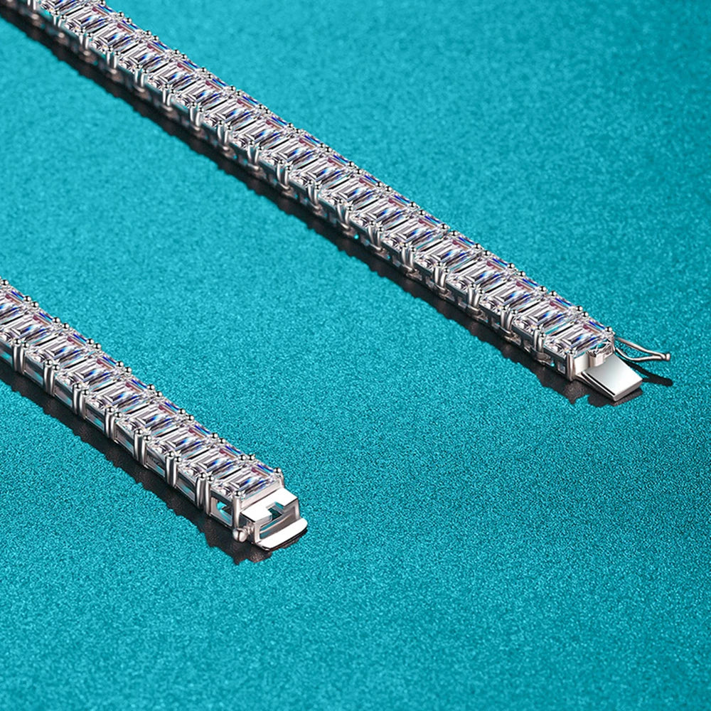 A close-up studio shot of a silver tennis bracelet with rectangular blue gemstones, shown in two parallel diagonal segments on a textured turquoise background.