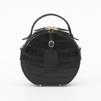 A black crocodile-embossed leather handbag with a top handle, gold-tone hardware, and a front hanging tag, photographed on a clean white background.
