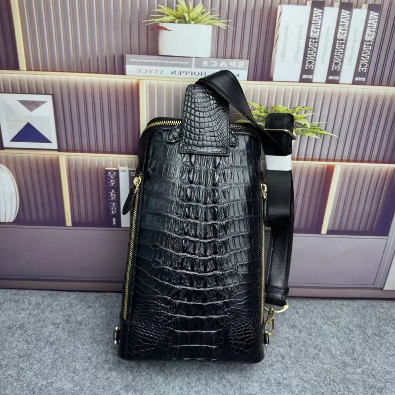 A black crocodile-embossed leather shoulder bag with gold-tone zippers and hardware, standing upright against a decorative bookshelf background.