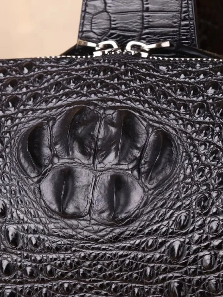 Close-up of a black crocodile-embossed leather handbag showing a raised alligator claw pattern and silver zipper hardware.