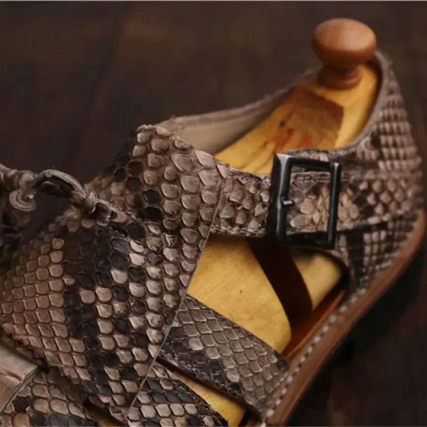 A close-up of a snakeskin-patterned clog shoe with a wooden shoe tree insert, set against a dark wooden background.