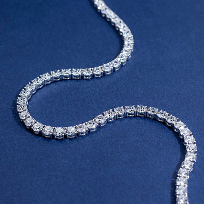 A silver tennis bracelet paved with clear round-cut gemstones, arranged in a curved S-shape on a textured dark blue background.