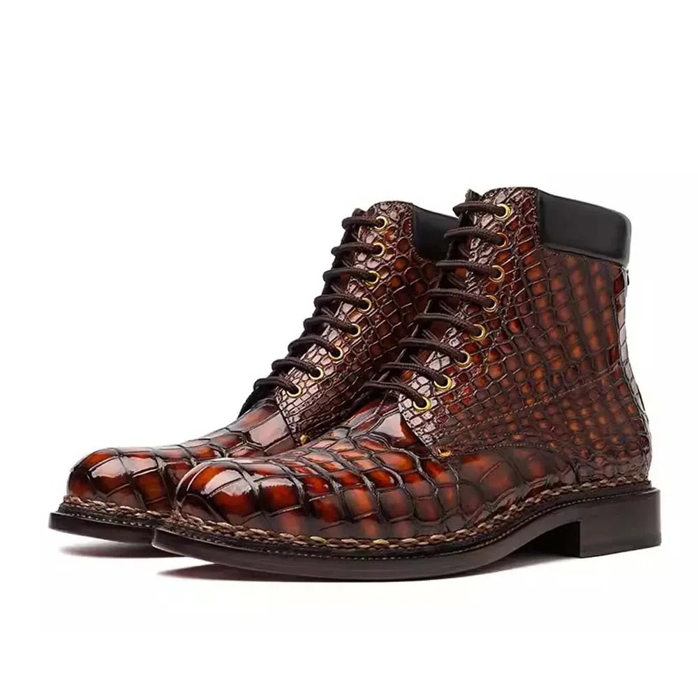 A pair of men's lace-up ankle boots featuring a glossy brown crocodile skin texture, dark brown laces, and a black heel, shown against a plain white background.