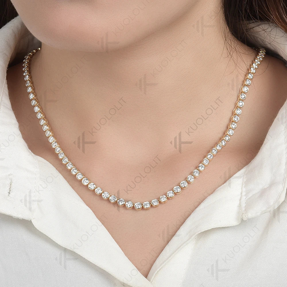 A close-up of a model wearing a delicate gold tennis necklace set with clear round-cut gemstones, styled with a white collared shirt.