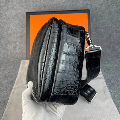 A glossy black crocodile-embossed leather shoulder bag held by a white gloved hand, with a bright orange box in the background.