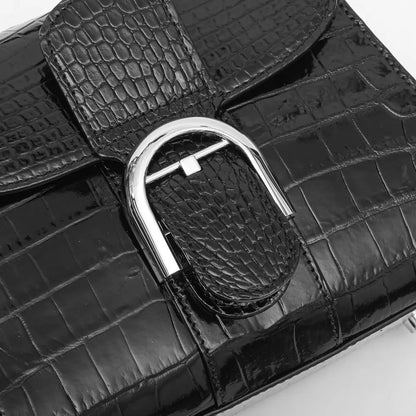 Close-up of a black crocodile-embossed leather handbag featuring a large silver-toned metal D-ring clasp and a matching strap detail.