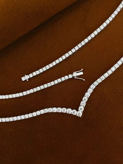A silver-toned tennis necklace paved with clear stones, displayed on a textured brown suede-like surface.