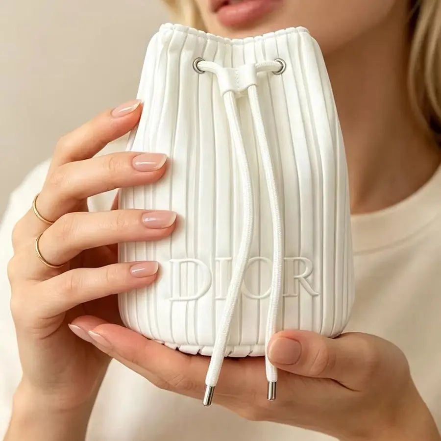 A close-up of a person holding a white pleated drawstring bucket bag with the embossed brand name DIOR on the front.