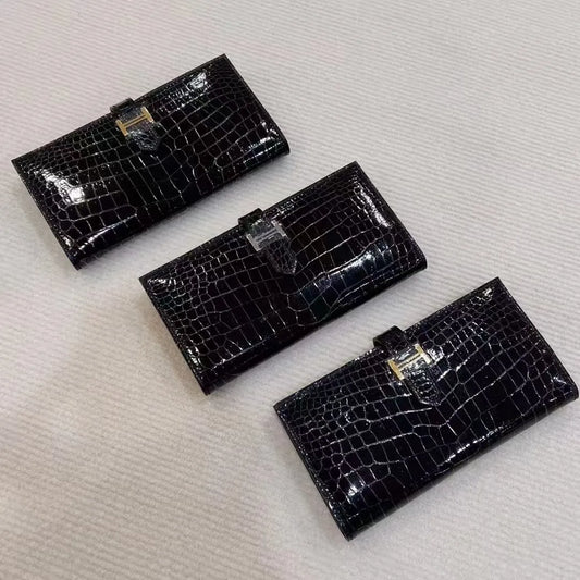 Three black crocodile-embossed leather bifold wallets arranged diagonally on a textured off-white fabric background.