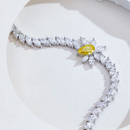 A silver-toned curved necklace featuring marquise-cut clear stones and a central yellow pear-cut gemstone surrounded by small clear stones, displayed on a white surface.
