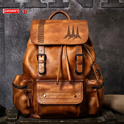 A brown leather backpack with multiple front pockets, buckle details, and an embossed bat logo on the flap, displayed against a dark textured wall.
